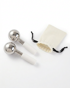 Two facial ice globes beside a cream drawstring storage pouch on white