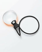 Black neck magnifier laid flat on white showing lens and looped neckband