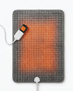 Electric heating pad laid flat with warm orange glow and digital controller