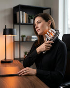 Woman using the handheld massager on her neck at a home office desk