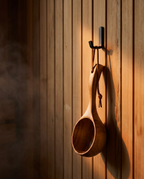 Wooden sauna ladle hanging from a wall hook on cedar paneling