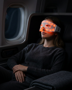 Woman on a plane wearing the glowing red light eye mask while resting