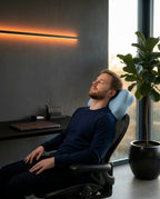 Man napping in an office chair resting on the blue contour pillow by a window