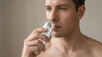 Man using the white nose and ear trimmer near his nostril, bare shoulders