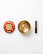 What's-in-the-box flat lay: singing bowl, red silk cushion and wooden striker