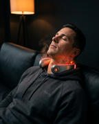 Man unwinding on a couch wearing the glowing red-light neck massager