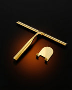 Brass shower squeegee and wall hook laid flat on a dark glowing surface