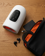 Hand massager with travel pouch, charger and earbuds on a wooden surface