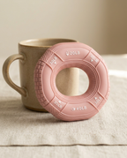 Pink grip strengthener ring leaning against a ceramic mug on linen