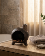 Ceramic ritual burner smoking on a stone spa shelf beside folded towels