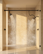 Two black shower heads spraying inside a sunlit marble walk-in shower