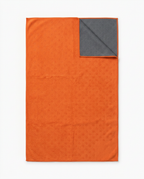 Orange yoga towel with corner folded to reveal gray grip-dot backing