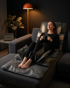 Woman relaxing on the massage mat over a sofa, holding a mug at night