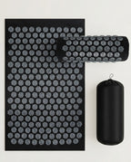 Grey acupressure mat with rolled pillow and carry bag on white