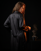 Woman from behind in a black satin robe with a steaming mug, wind-down