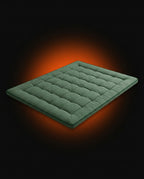 Sage green quilted floor mattress on a dark backdrop with orange glow