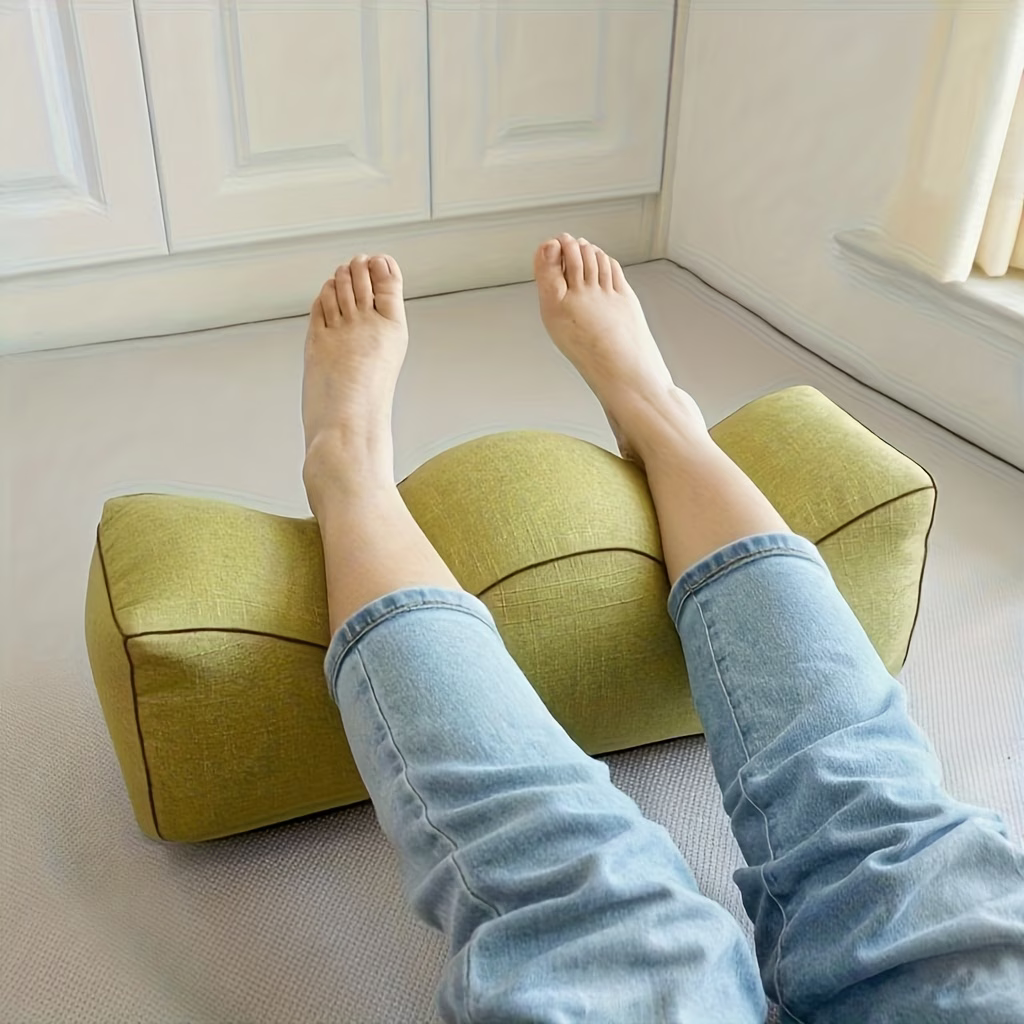 Person resting their legs over a green wedge leg support pillow on the floor