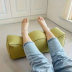 Person resting their legs over a green wedge leg support pillow on the floor