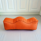 Orange linen leg support pillow with wavy contoured top, side view